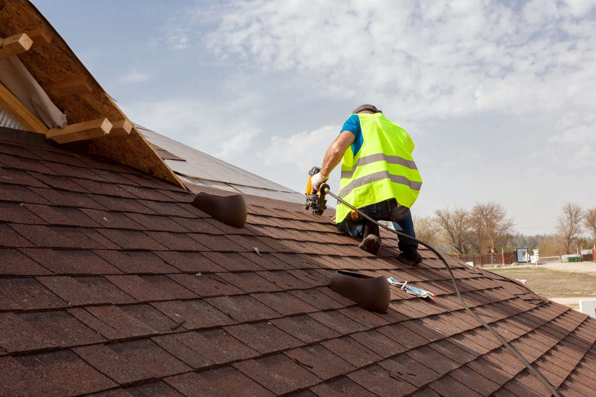 Roofer installing box vents near the ridge of an asphalt shingle roof — attic exhaust ventilation sized to the 1/150 and 1/300 rule