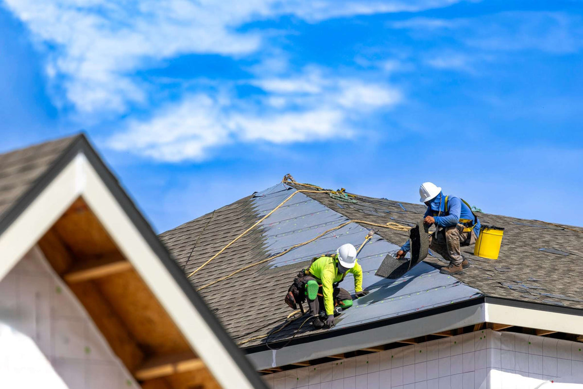 Roofing crew rolling out gray synthetic underlayment on a residential roof deck — synthetic underlayment vs felt paper