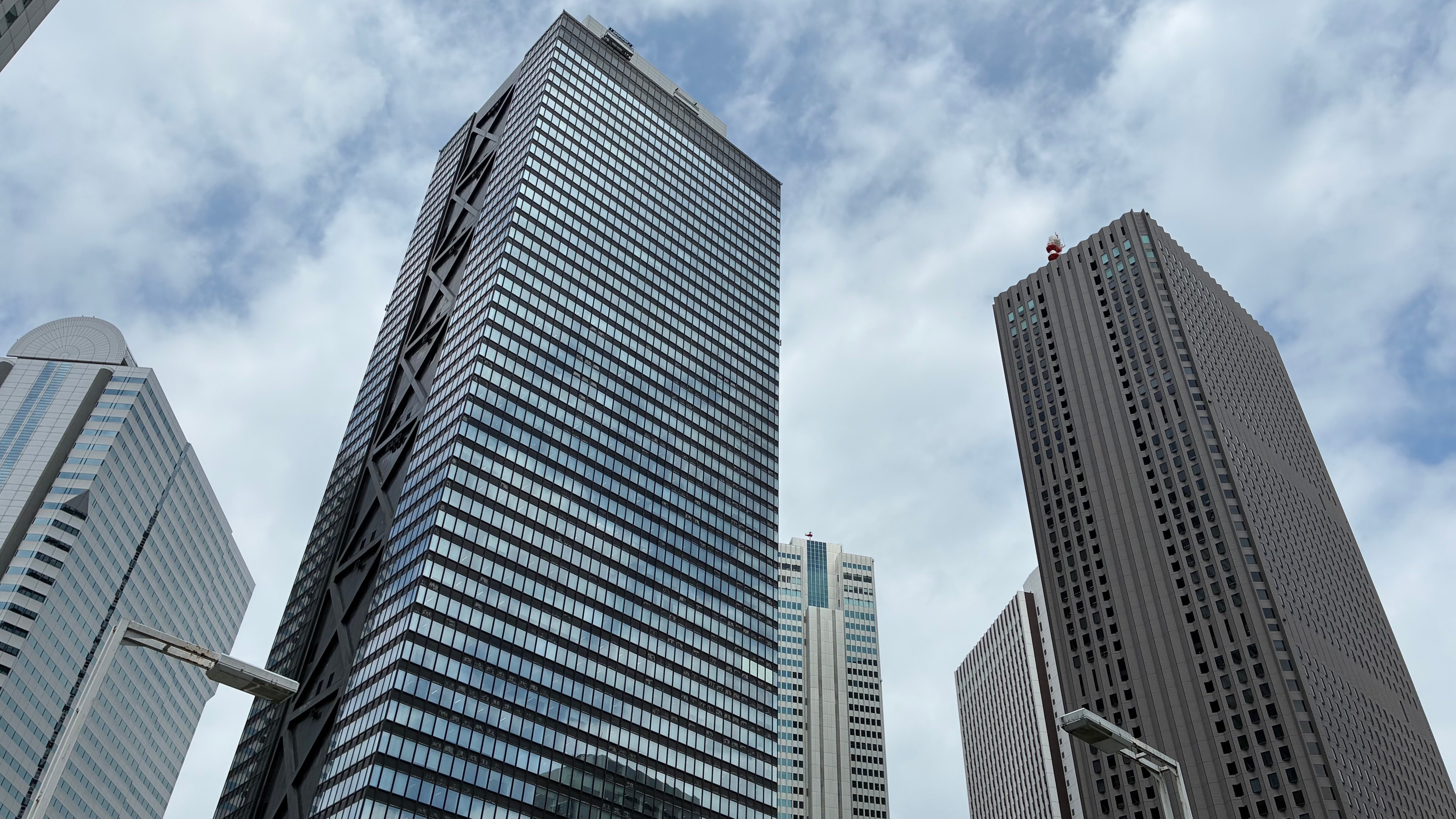 Two towering office buildings connected by a single bridge shaped like a residential roof, with a tug-of-war rope stretched between the buildings and a gavel resting on the roofline — corporate fight over the roofing middle ground
